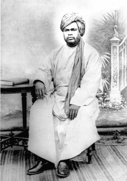Seated w arm resting on table, with turban