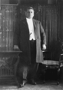 Standing, left hand on table, waist coat