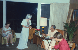 Swami Swahananda sits in a chair behind a tv dinner tray with some nuns as Sister Shaktiprana stands before him