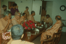 Many Swamis at the dining table, Swami Aseshananda at the head, with Swamis Tadatmananda, Bhadrananda, Swananda, Swahananda, Unknown, Prabuddhananda, background Yogaprana, Amrita (Monica Salm), Anandaprana